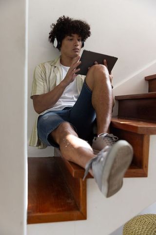 Young Man Relaxing on Stairs with Tablet and Headphones at Home