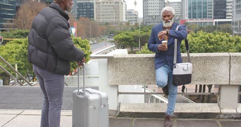 Senior african american men waiting at urban plaza with luggage and coffee checking watch