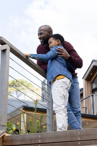 African american father and son leaning on deck railing smiling, sharing warm moment