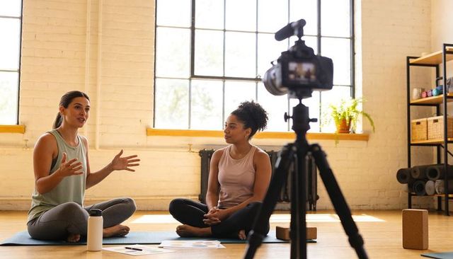 Recording yoga coaching session with two instructors on mats in sunlit brick studio