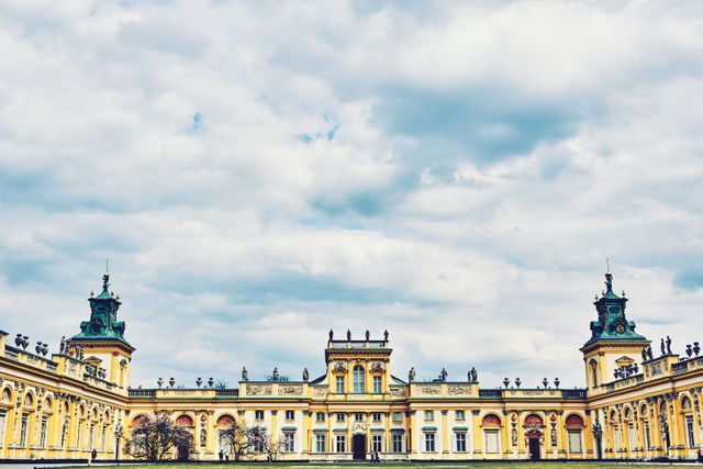 Beautiful exterior view of a grand royal palace showcasing detailed baroque architecture against a backdrop of a blue, slightly cloudy sky. Great for use in travel brochures, architecture magazines, and educational materials about historical landmarks. The image captures the grandeur and majestic presence of the historical building, making it ideal for advertisements targeting tourism and cultural heritage enthusiasts.
