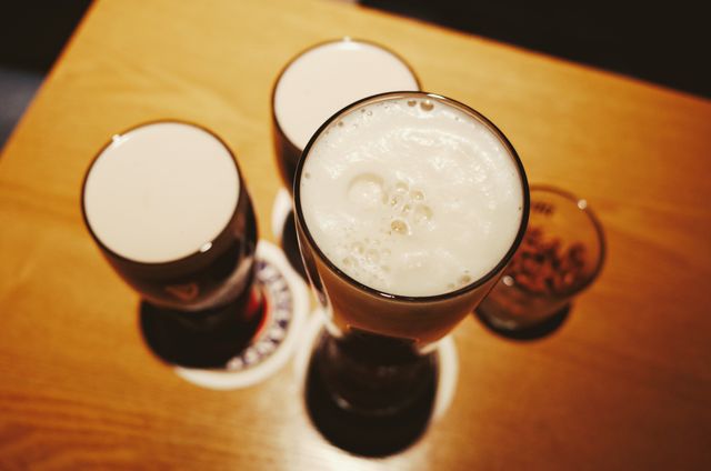 Four glasses of frothy beers placed on a wooden table, seen from above. Ideal for illustrating social gatherings, bar environments, and leisure activities. Suitable for advertising beer, pubs, or nightlife scenes.