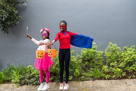 African american preteen girls in halloween costumes holding jack-o'-lantern buckets on sidewalk