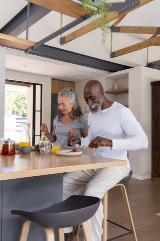 Senior couple enjoying bright contemporary open-plan kitchen breakfast at wooden island