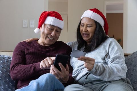 Joyful senior couple shopping online with smartphone at christmas