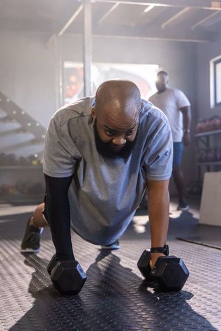African american man performing dumbbell push-ups with coach spotting in gym