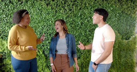 Diverse friends laughing and chatting outdoors by lush green hedge casual lifestyle scene