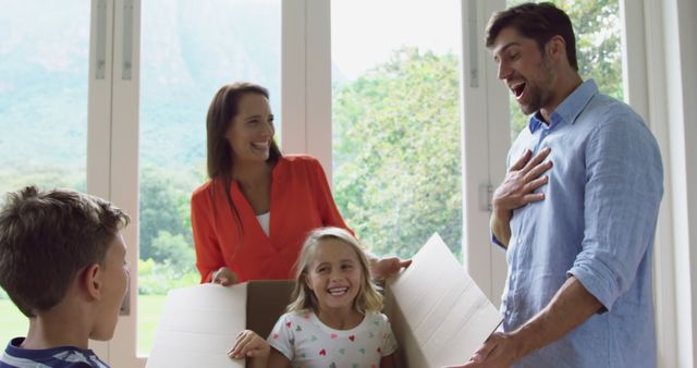 A family, consisting of parents and young children, is joyfully unpacking cardboard boxes in their new home. Everyone is smiling, conveying happiness and excitement about moving in. This scene suggests family bonding, new beginnings, and positive emotions, making it perfect for advertisements or articles related to moving, real estate, family life, and joyous occasions.