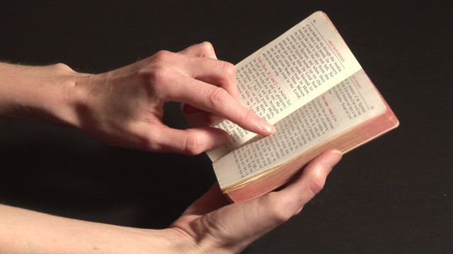 Pair of hands carefully holding and reading a small religious book, showcasing a sense of concentration and reverence. This can perfectly suit editorial designs, religious blogs, educational content, or class about spiritual practices. Great for any communication portraying thoughtful engagement with literature.