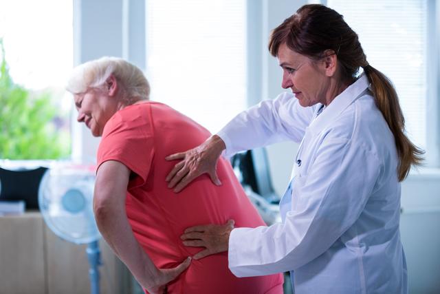 Female doctor examining senior patient experiencing back pain in a hospital setting. Useful for content related to healthcare, elderly care, medical examinations, physical therapy, and patient-doctor interactions.
