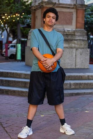 Young african american man holding basketball at urban plaza with string lights at dusk