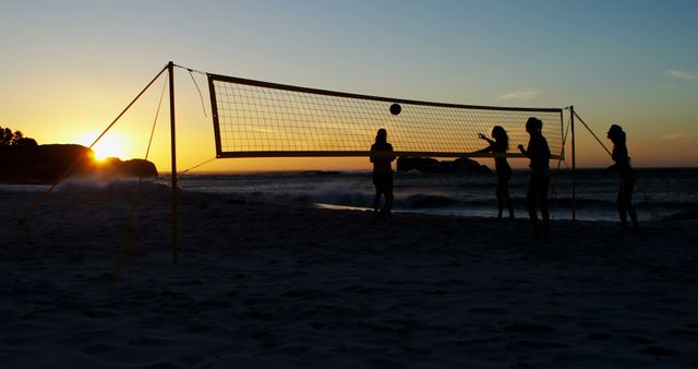 Silhouetted people play beach volleyball at sunset, with copy space. The game adds a dynamic vibe to the serene beach setting.