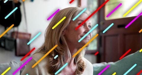 Smiling mature woman sitting on sofa with colorful diagonal streak overlay, home portrait