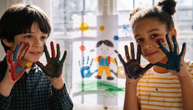 Sunlit classroom kids showing colorful painted hands, smiling and collaborating in art activity