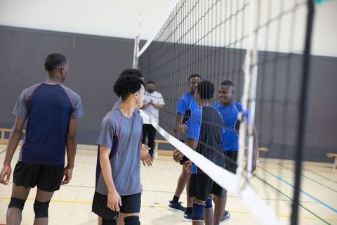 Teen male volleyball teams shaking hands across net in school gym showing sportsmanship