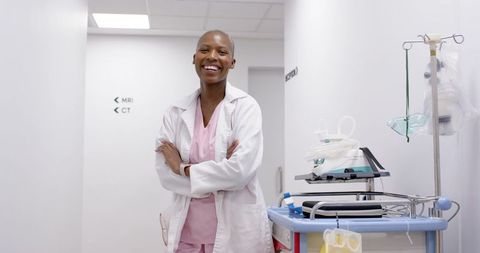 African female clinician smiling while standing beside medical cart in mri ct corridor
