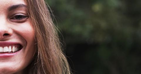 Woman Smiling Outdoors with Lush Greenery in Background