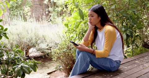 Woman Relaxing on Garden Bench Holding Smartphone Outdoors