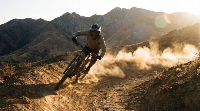 Mountain biker carving singletrack kicking dust at golden hour in rugged desert hills