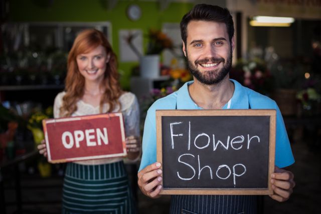 Man holding slate with flower shop sign and woman holding open signboard