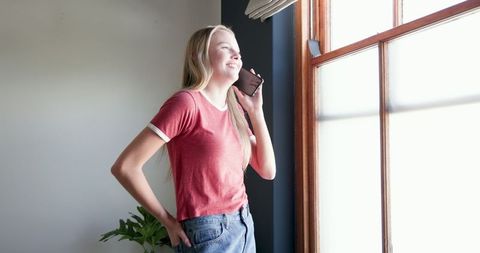 Teen Girl Communicates Happily on Smartphone by Window