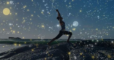 Woman Practicing Yoga Lunge on Rocky Shore at Dusk with Sparkling Bokeh Sky