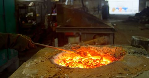 Foundry worker melting metal in factory furnace
