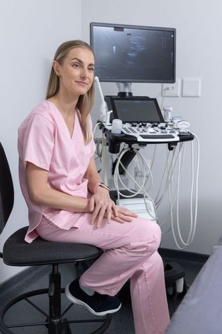 Female sonographer sitting in pink scrubs using ultrasound machine in clinic