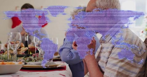 Senior man touching face at family dinner with holographic world map overlay