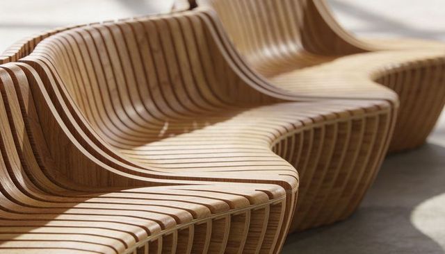 Curving sculptural wooden bench with slatted laminated timber seats and sunlit shadows
