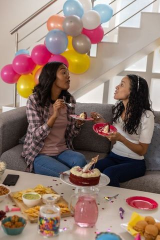 Diverse friends celebrating with cake on couch at colorful balloon party