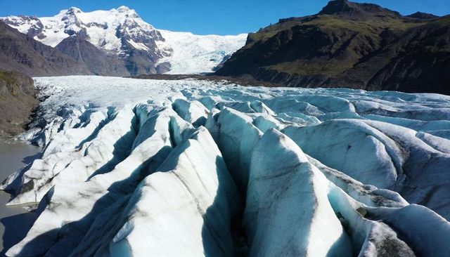 Glacier tongue flowing through alpine valley with deep crevasses, blue-ice and moraines