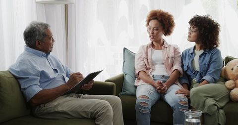 Senior therapist conducting counseling session with diverse women on living room sofa
