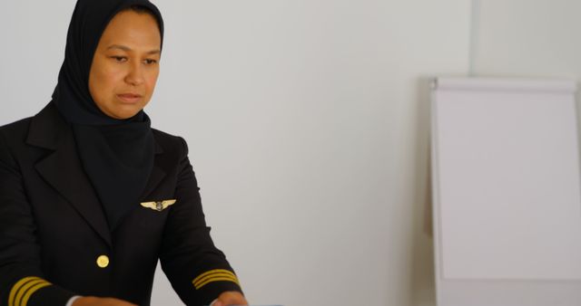 A middle-aged Asian woman in a pilot uniform is focused on her task, with copy space. Her professional attire and demeanor suggest she is preparing for a flight or reviewing important documents.