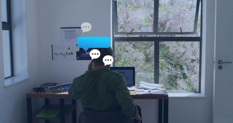 Remote professional talking on phone while checking laptop at bright home office desk