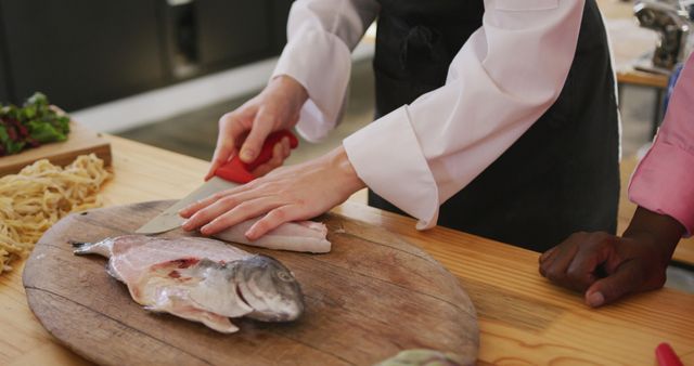 Midsection of caucasian female cook slicing fish on cutting board in kitchen. Lifestyle, food, cooking and senior lifestyle, unaltered.