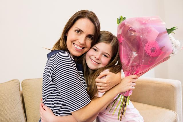 Mother and daughter sharing a heartfelt moment in the living room. The daughter is giving her mother a flower bouquet, symbolizing love and appreciation. Perfect for use in family-oriented advertisements, Mother's Day promotions, and articles about family bonding and celebrations.