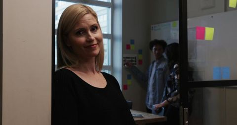 Blonde Woman Smiling in Office Doorway with Colleagues Collaborating