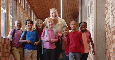 Diverse schoolchildren and teacher in bright corridor with backpacks