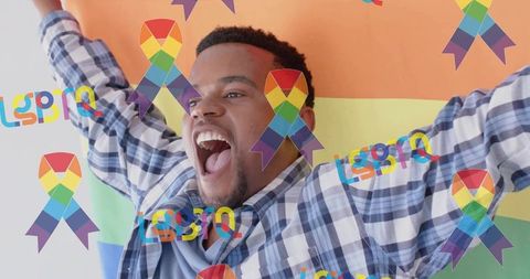 Man celebrating pride raising arms in front of rainbow flag with lgbtq ribbons