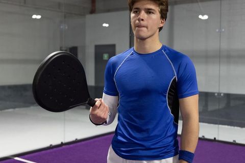 Focused young athlete standing on indoor padel court holding paddle preparing to serve