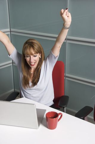 Cheerful Businesswoman Celebrates Success at Desk with Laptop