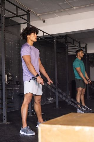 Hispanic men performing battle rope workout beside plyo box in industrial gym, building strength