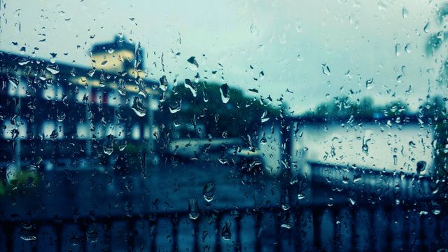 View of a wet window covered with raindrops, making an urban landscape blurry during a rainy day. Ideal for depicting melancholic weather, urban scenes, or concepts of isolation and calmness in advertisements, website designs, or blogs. Can also be used in backgrounds and overlays to convey moodiness and serenity.