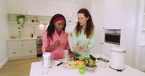 Diverse friends preparing healthy smoothie together in modern kitchen