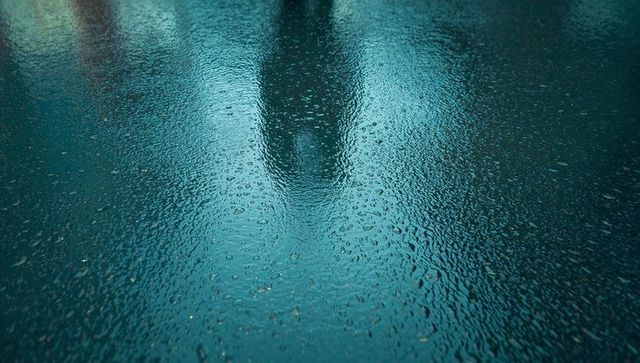 Raindrops on wet asphalt creating reflective puddles