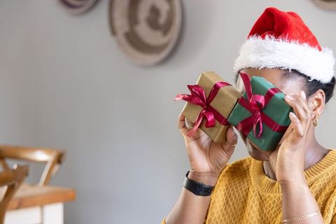African american woman wearing santa hat holding wrapped gifts in cozy dining area