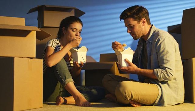 Couple unpacking and eating takeout amid moving boxes, cozy late-night meal