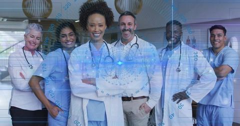 Standing multicultural medical team wearing lab coats and scrubs in hospital corridor