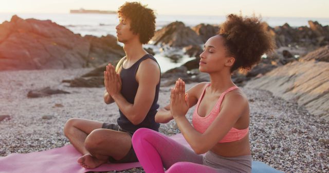 African american couple practicing yoga and meditating together on rocks near the sea during sunset - Download Free Stock Photos Pikwizard.com